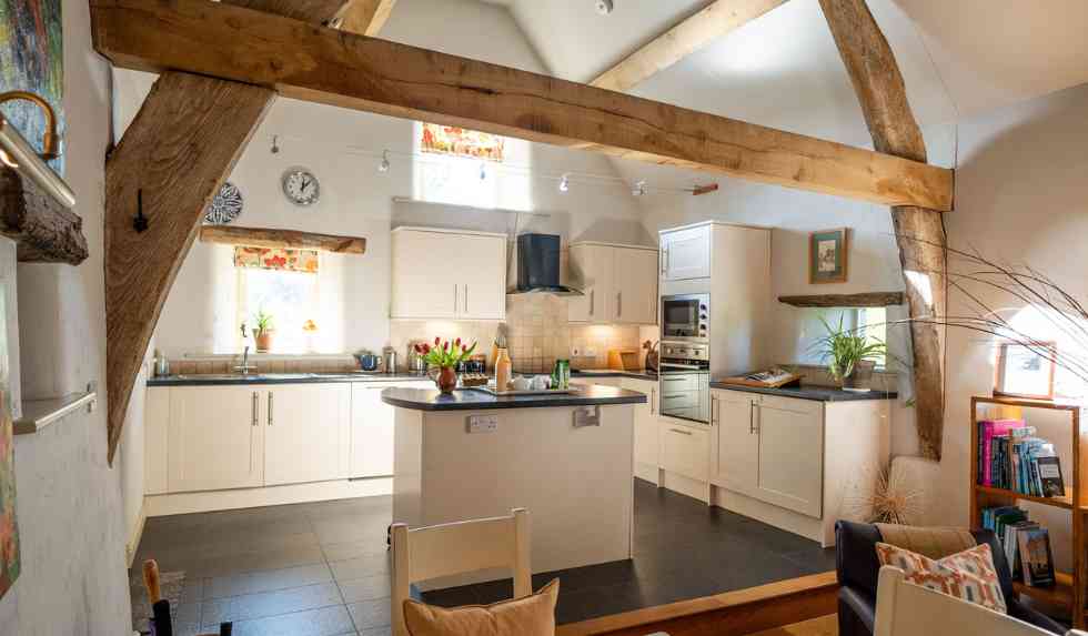 Light, modern, open plan country kitchen featuring arched cruck beams and flooded with sunlight. 