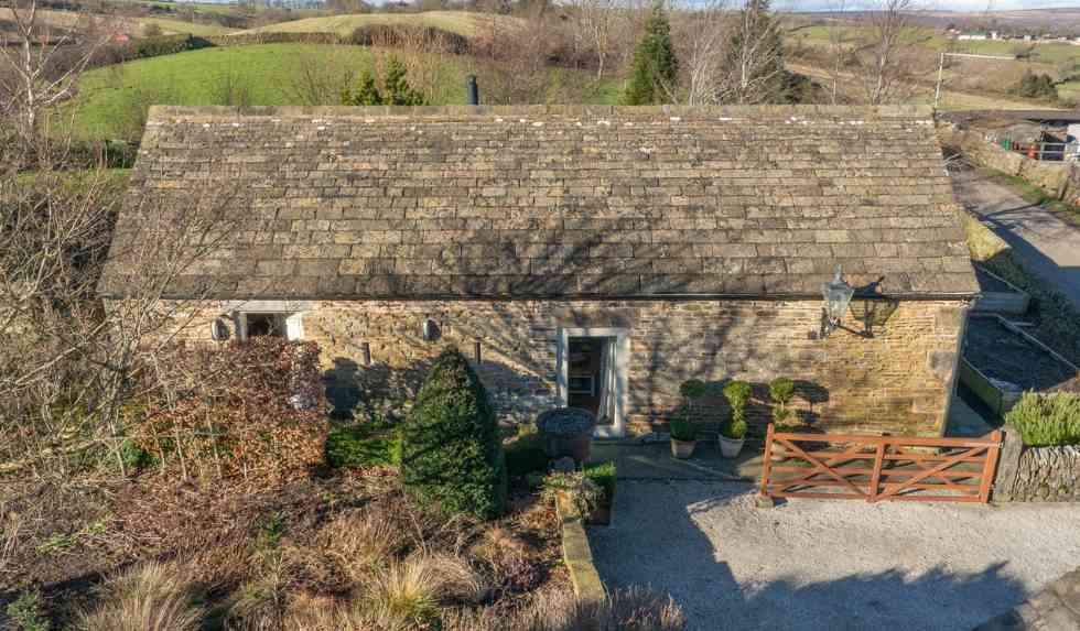 Charming stone exterior of Cruck Barn Cottage in Derbyshire, surrounded by countryside views and a wooden gate entrance.