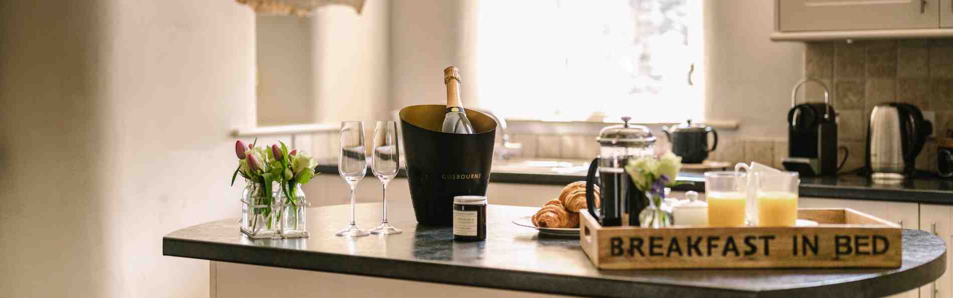 A kitchen island laid with dainty vases of beautiful flowers, a bottle of prosseco with glasses and tea and coffee tray.